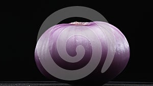 Macrography of peeled red onion against a sleek black background. Comestible.