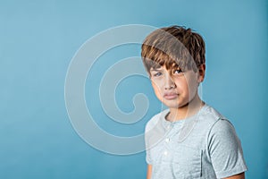 A mad angry pre-teen tween boy from the shoulders up on a muted blue backdrop