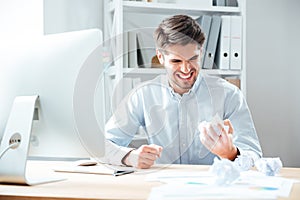 Mad annoyed businessman working and crumpling paper in office