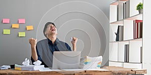 Mad crazy man employee sitting in office workplace with sticky notes all around, shouting furious angry, pissed off