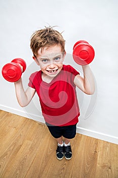 Mad frowning boy expressing rage and motivation raising dumbbells