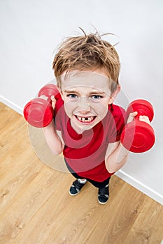 Mad frowning boy with loose tooth raising dumbbells with effort