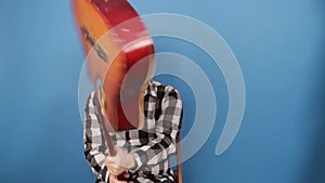A mad man hits himself on the head with a guitar. The guy breaks a guitar on his head on a blue background.