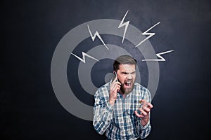 Mad man using cell phone and screaming over blackboard background