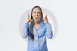 Mad outraged asian girl in blue pajamas arguing, having argument with girlfriend during sleepover, swearing or cursing