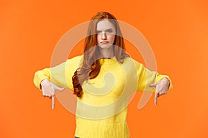 Mad unsatisfied cute redhead girlfriend, ginger girl in yellow sweater, frowning disappointed and angry, pointing down