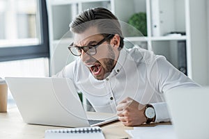 mad young businessman shouting at laptop