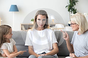 Mad young mom sit between grandmother and daughter scolding her