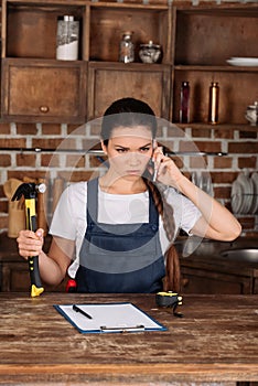 mad young repairwoman with hammer talking by phone