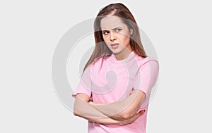 Mad young woman has upset facial expression, wears pink casual outfit, keeps crossed hands on waist, isolated over white studio