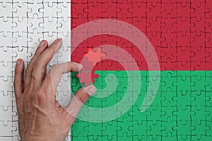 Madagascar flag is depicted on a puzzle, which the man`s hand completes to fold