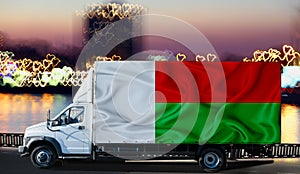 Madagascar flag on the side of a white van against the backdrop of a blurred city and river. Logistics concept