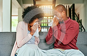 We made each other sick. a young couple blowing their noses at home.