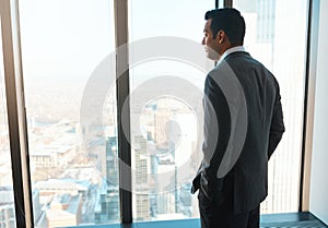 He made it to the top. a young businessman looking out the window in an office.