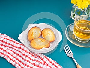 Madeleine homemade traditional French small cookies on black a dish with a cloth and a cup of tea placed on a blue light