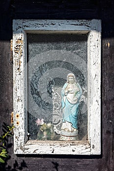 Madonna statue in the window of old wooden cottage