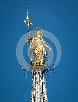 Madonnina atop Milan Cathedral at the height of 108.5 m in Milan, Italy. Golden statue of Madonna close-up on the blue sky