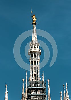 Madonnina atop Milan Cathedral at the height of 108.5 m in Milan, Italy. Golden statue of Madonna on spire on the blue sky