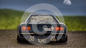 Model of a navy blue Ferrari GTO car seen from behind on the asphalt with a mountain of grass and a blue sky with the evening moon