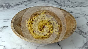 Mafaldine corte pasta falling into wooden bowl. Marble worktop background