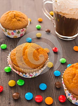 Mafins on a wooden table, beside scattered multi-colored tablets. Delicious dessert with a blurry background. Festive