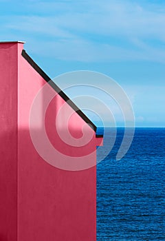 Magenta wall of building with a sea and sky background.