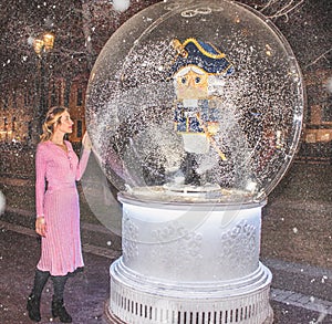 Magic ball with a nutcracker inside and a ballerina girl in a pink shining dress next to it on a snowy background