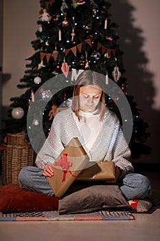 The Magic Of Christmas. Amazed young beautiful woman opening xmas gift box with light inside, sitting on floor near