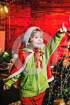 Magic Christmas night for kids. Happy excited smiling boy with pointing finger by the Christmas tree. Little kid is