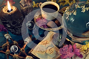 Magic crystal ball, skull candle and runes on altar ritual table.