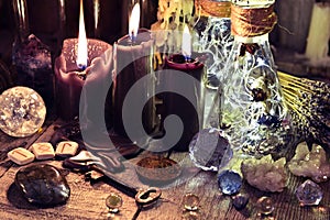 Magic crystals, ritual objects, runes, black candles and bottles on witch table