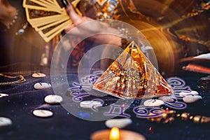 Magic divination and esotericism. Magic glass pyramid with a magical glow. In the background, a fortune teller holds a fan of