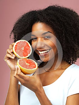 The magic is inside. Studio shot of an attractive young woman eating grapefruit against a pink background.