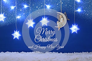 Magical christmas image of little white fairy with glitter wings sitting on the moon over blue background and silver snowflake gar