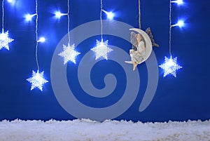 Magical christmas image of little white fairy with glitter wings sitting on the moon over blue background and silver snowflake gar