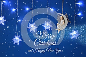 Magical christmas image of little white fairy with glitter wings sitting on the moon over blue background and silver snowflake gar