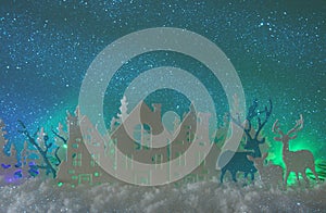 Magical Christmas paper cut winter background landscape with houses, trees, deer and snow in front of northern lights background.