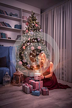 Magical look of a woman near a Christmas tree delighted with a measured Christmas present on New Year`s Eve. surprise, magic,