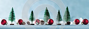 Magical miniature winter wonderland banner. Evergreen trees, pine cones and red christmas baubles on shiny blue background.