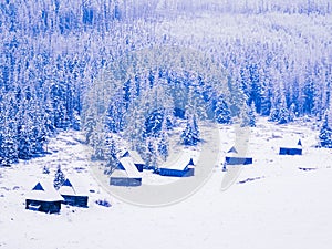 Magical mountain winter landscape, wooden houses and pine trees covered with snow