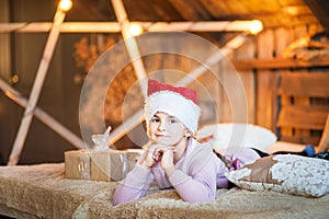 A magical photo of a little girl at home on the bed under Christmas. Portrait of a girl in a pink sweater close-up with a hat of S