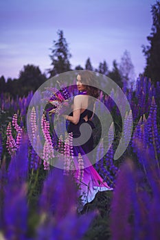 A magical portrait of a young girl in a gradient dress in a purple-pink lupine field at night.