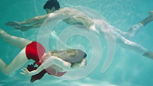 Magical underwater shot of young woman in red dress and man swimming underwater. Couple swims past each other moving