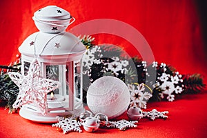 Magical white lantern is standing with white knit star on it and a fir tree branch and a snowball on a christmas red background.