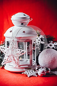 Magical white lantern is standing with white knit star on it and a fir tree branch and a snowball on a christmas red background.