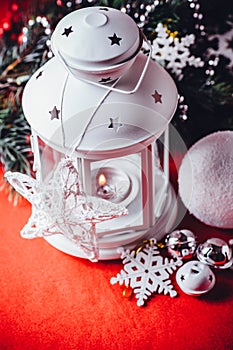 Magical white lantern is standing with white knit star on it and a fir tree branch and a snowball on a christmas red background.