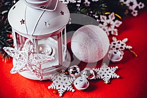 Magical white lantern is standing with white knit star on it and a fir tree branch and a snowball on a christmas red background.