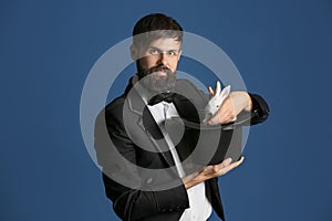 Magician holding hat with rabbit on color background