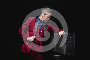 Magician man with magic wand and suitcase on black background