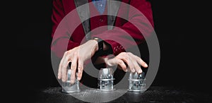 Magician shows shell game of thimbles with circles and ball, black background. Concept deception, sleight hand